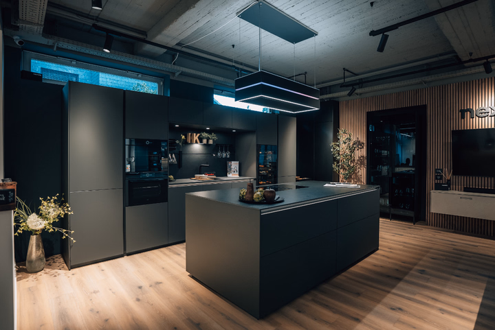 Gesamtansicht einer modernen High-End-Küche in dunklen Brauntönen mit zentraler Kochinsel und offener Regallösung im Küchenköpfe Showroom.
