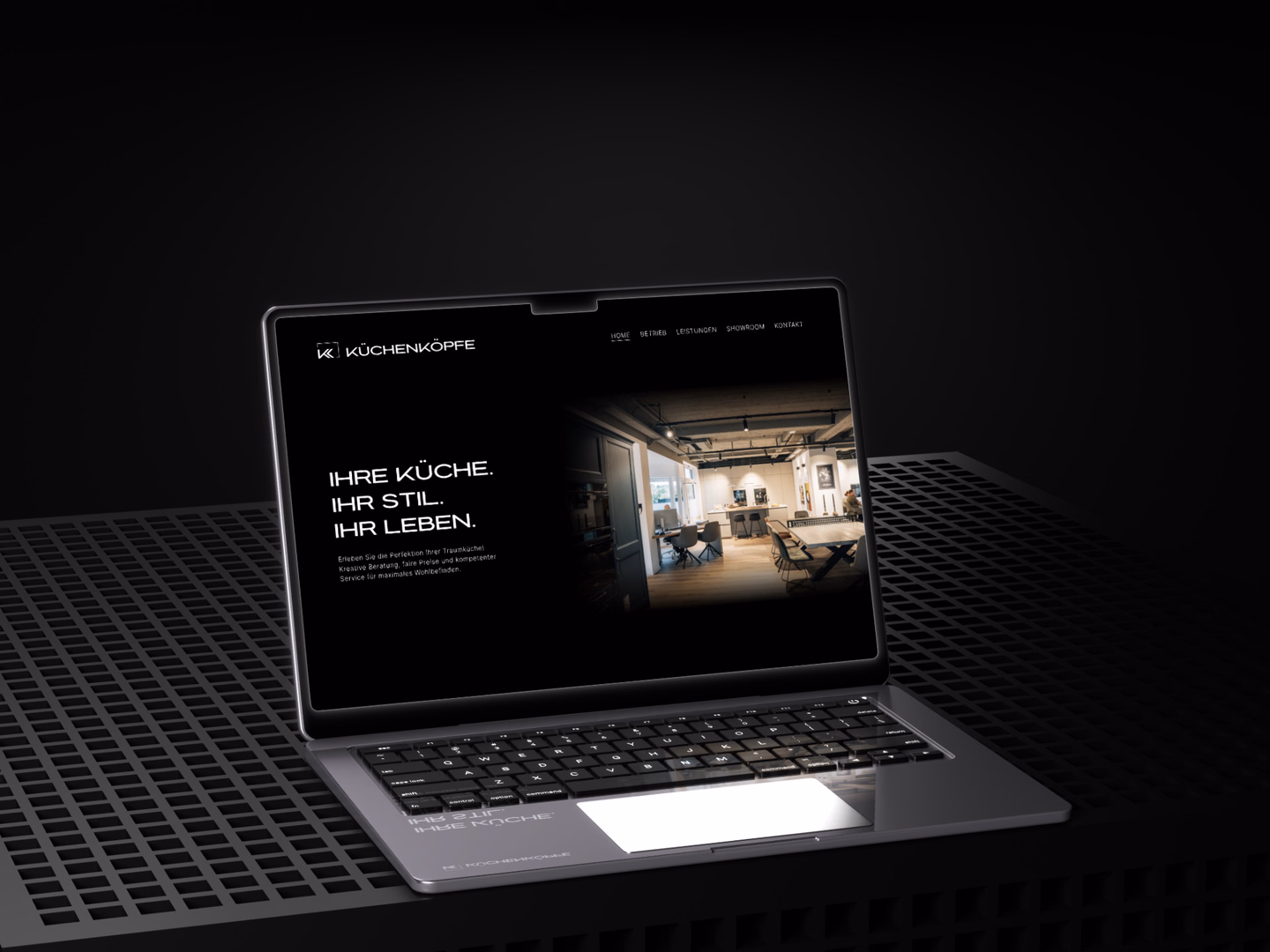 Ein hochwertiges Laptop-Mockup auf dunklem Industriegitter. Das Display zeigt die Startseite der Küchenköpfe-Website mit dem Slogan „Ihre Küche. Ihr Stil. Ihr Leben.“ und einer cleanen, dunklen Benutzeroberfläche.